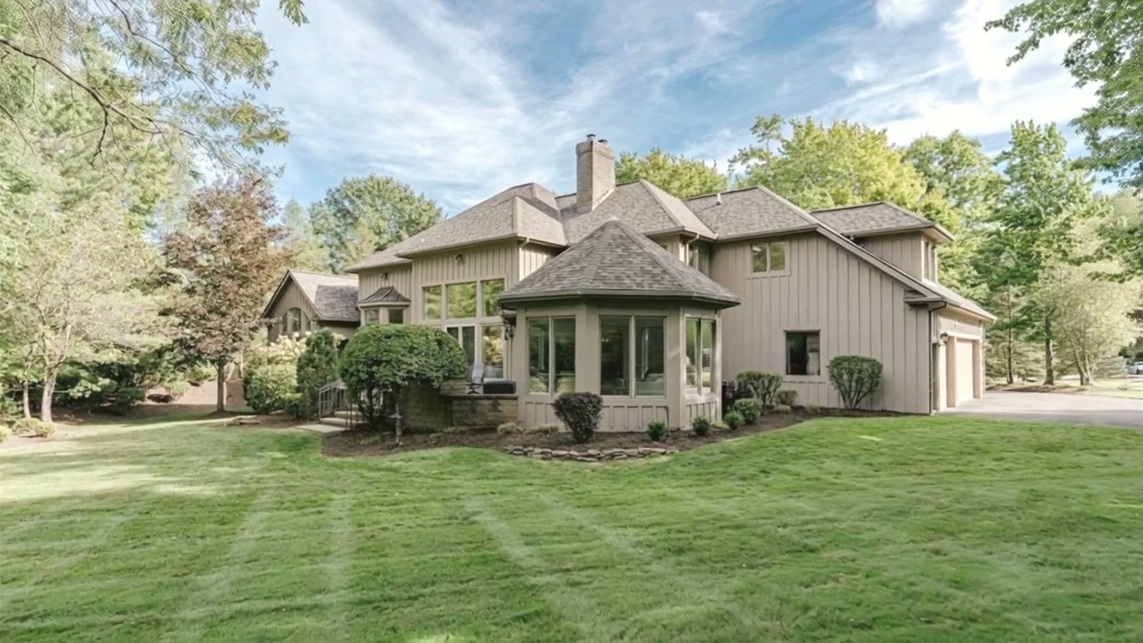 A stone and stucco contemporary home on a sunlit lawn among mature trees